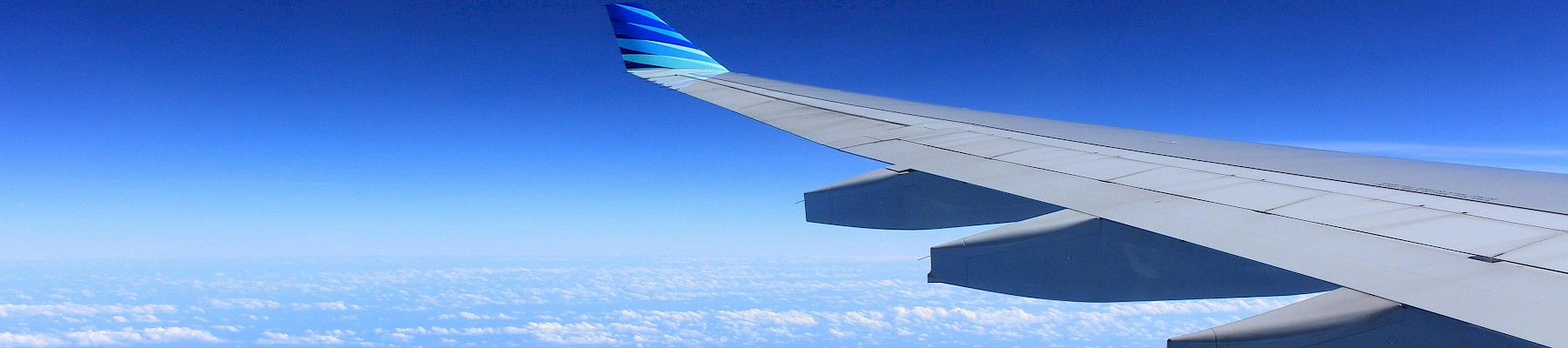 The image shows an airplane wing flying above clouds, high in the blue sky during a clear day.