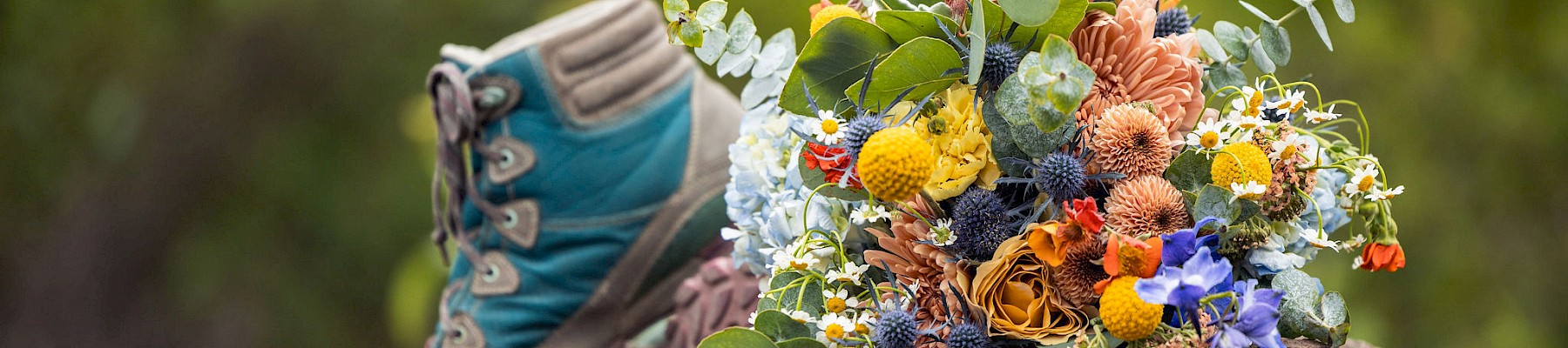 A hiking boot and a colorful bouquet of flowers placed on a rock outdoors with green blurred background.