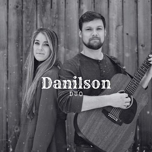 Male and female musicians standing back to back with acoustic guitar in front of wooden wall performing live music at Riverhouse Lodge in Bend Oregon