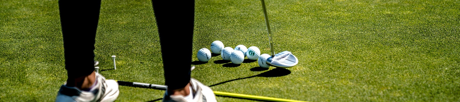 A golfer is preparing to hit the ball on a lush green golf course, surrounded by several golf balls, a club, and a measuring line.