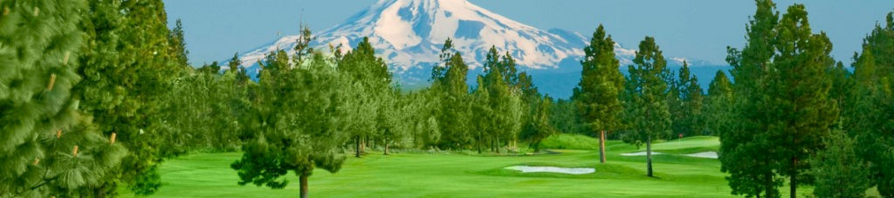 A picturesque golf course with a mountain and lush greenery in the background, featuring trees, a pond, and colorful flowers.