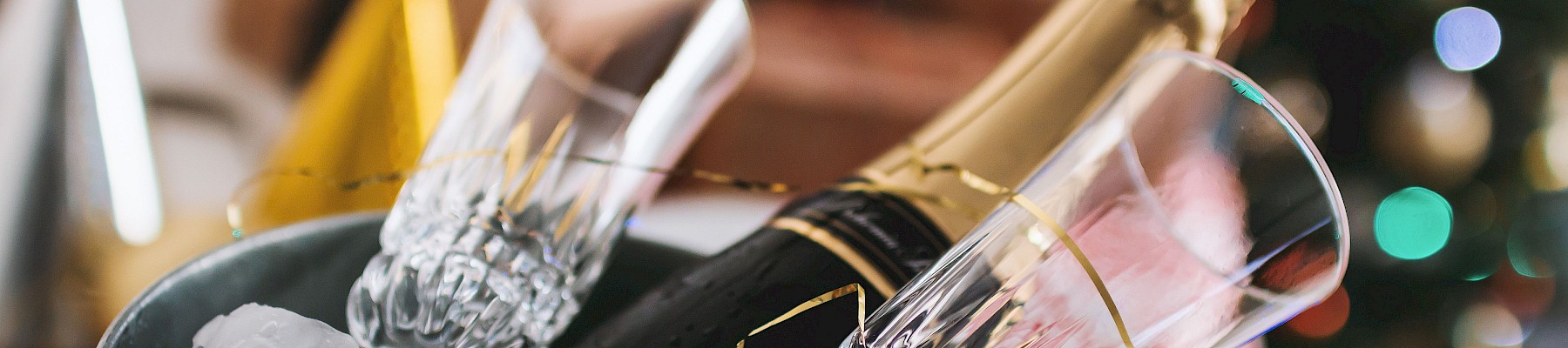 Champagne bottle with glasses in an ice bucket, festive scene, holiday lights in the background.