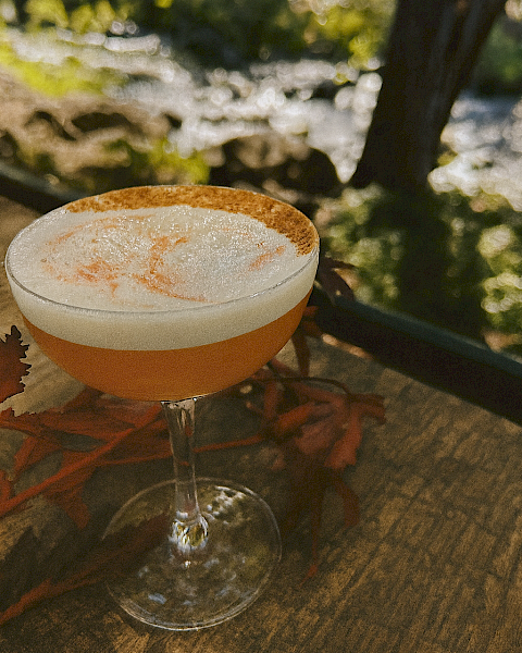 Golden Hour Sour cocktail with maple, bourbon, and cinnamon foam served on the riverside patio at Currents at Riverhouse Lodge in Bend Oregon during golden hour light.