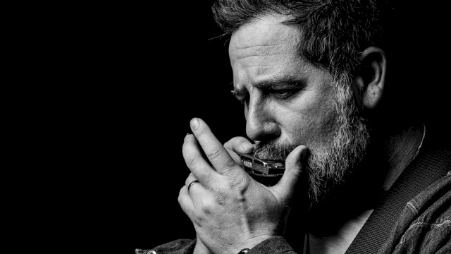 Black-and-white portrait of a singer-songwriter playing harmonica and acoustic guitar during a live performance at Currents at Riverhouse Lodge, a riverfront live music and dining venue in Bend, Oregon.