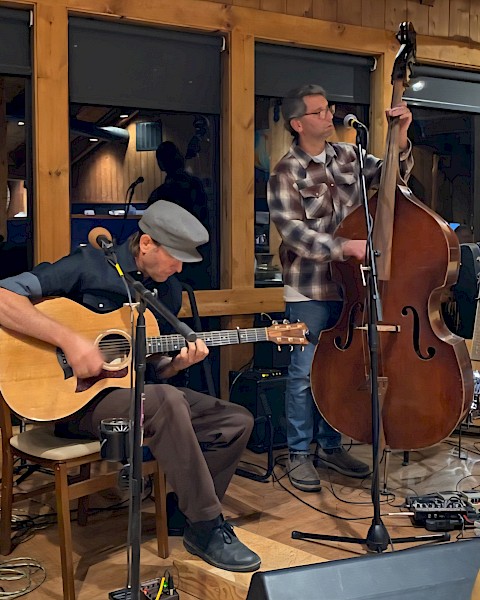 Two folk musicians performing live with acoustic guitar and upright bass during a brunch performance at Currents at Riverhouse Lodge, a riverfront live music venue in Bend, Oregon.