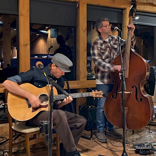 Two folk musicians performing live with acoustic guitar and upright bass during a brunch performance at Currents at Riverhouse Lodge, a riverfront live music venue in Bend, Oregon.