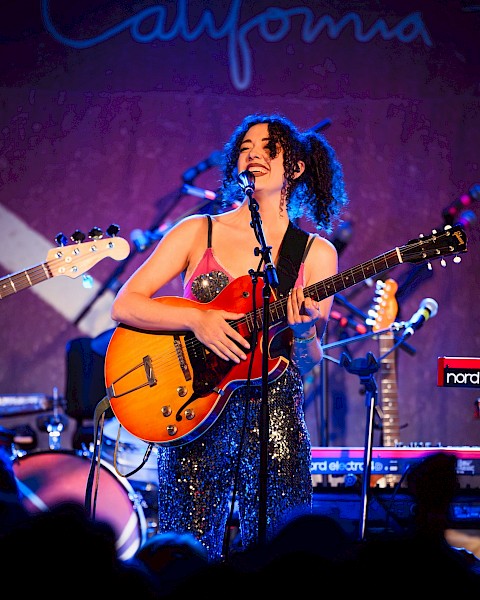 Female singer-songwriter performing live with electric guitar and microphone during Beats & Bites Brunch at Currents at Riverhouse Lodge in Bend, Oregon.