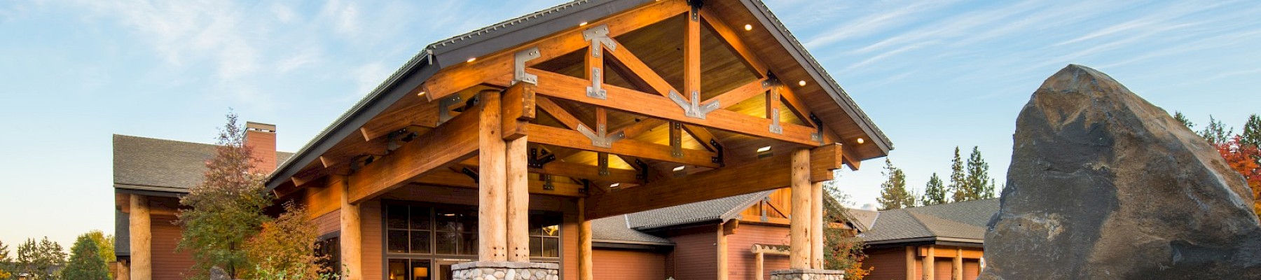 A large log and stone lodge with a landscaped garden in front, under a partly cloudy sky.