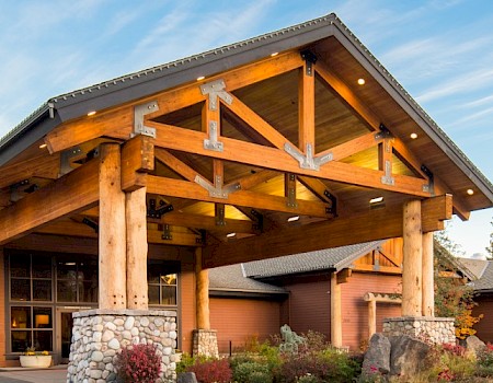 A large log and stone lodge with a landscaped garden in front, under a partly cloudy sky.