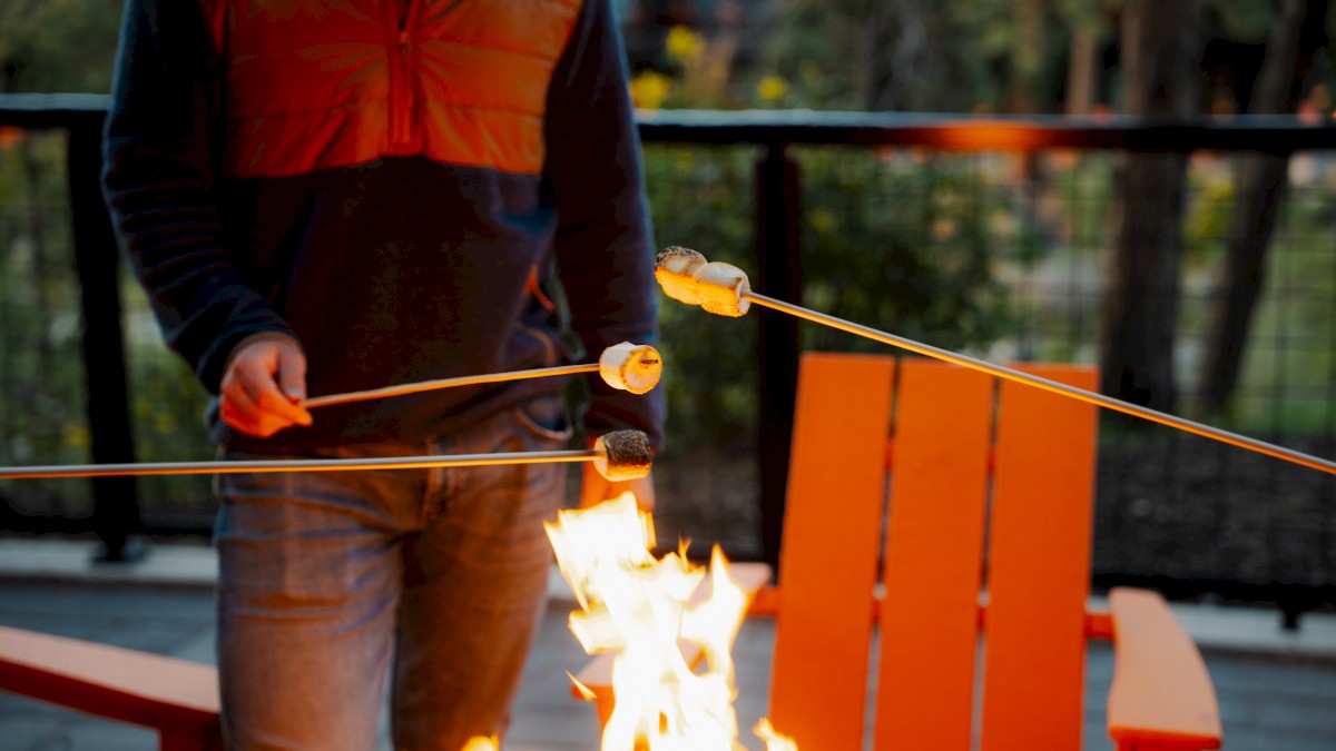 A person toasting marshmallows over a campfire on a wooden deck during the evening.