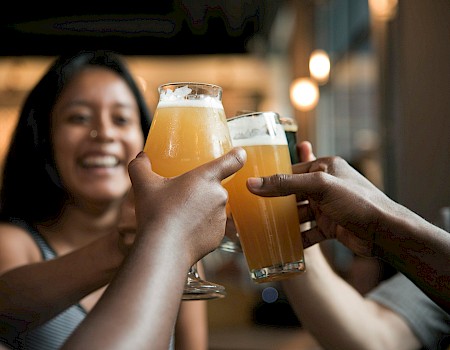 People are toasting with glasses of beer, celebrating together in a lively setting.