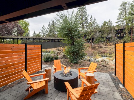 A cozy private outdoor patio with four orange Adirondack chairs gathered around a fire pit, surrounded by trees and a scenic Deschutes River at Riverhouse Lodge in Bend OR