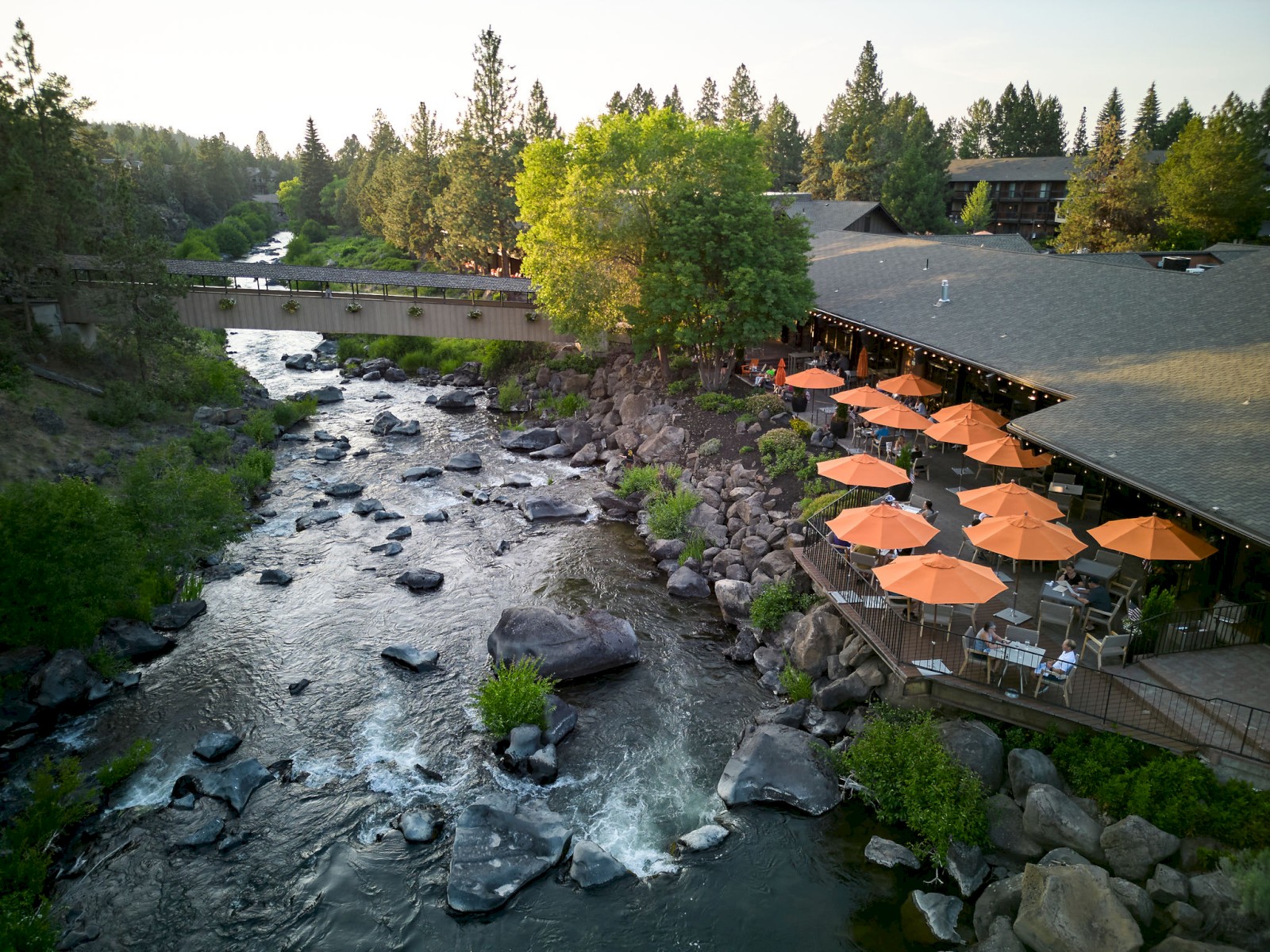 Riverhouse Lodge in Bend Oregon along the Deschutes River with outdoor patio dining, scenic footbridge, and spring landscape at riverside hotel resort in Central Oregon