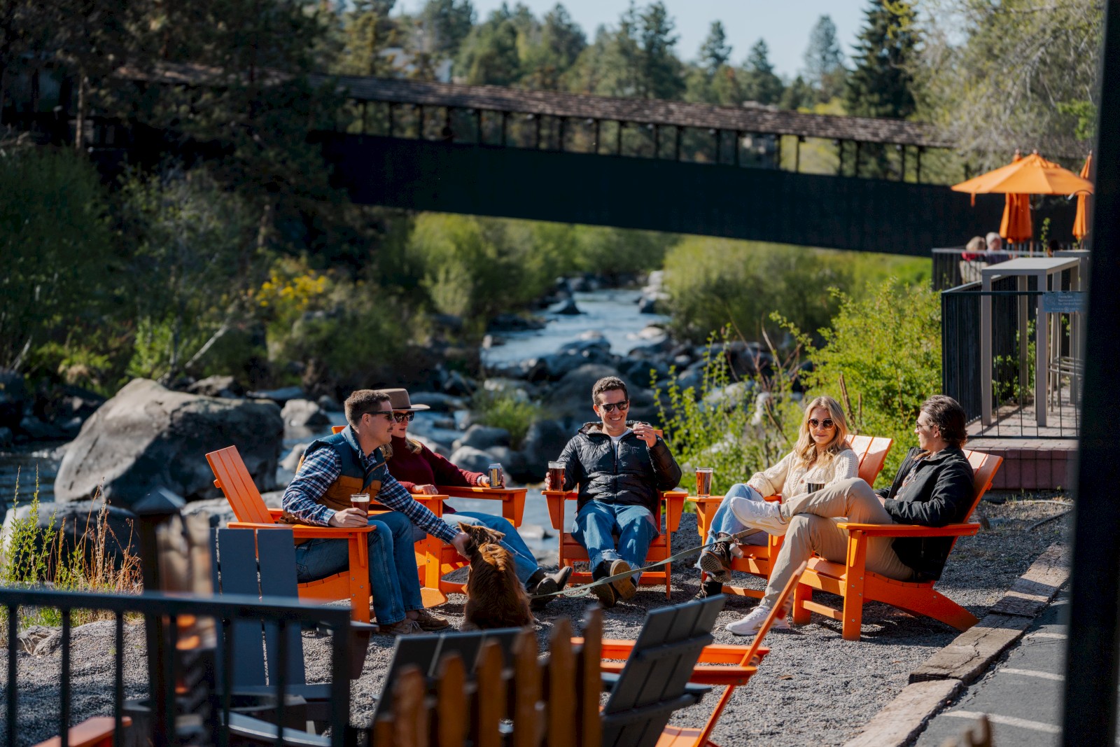 Riverfront relaxation at Riverhouse Lodge Bend Oregon with guests enjoying outdoor seating and drinks along the Deschutes River in Central Oregon
