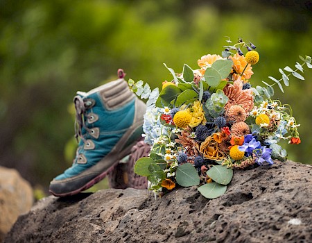 A hiking boot and a colorful bouquet of flowers placed on a rock outdoors with green blurred background.