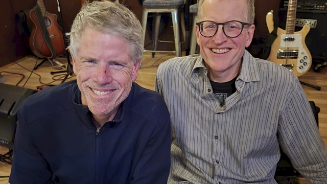 Two male musicians seated indoors with guitars and bass performing acoustic live music at a restaurant stage in Bend Oregon