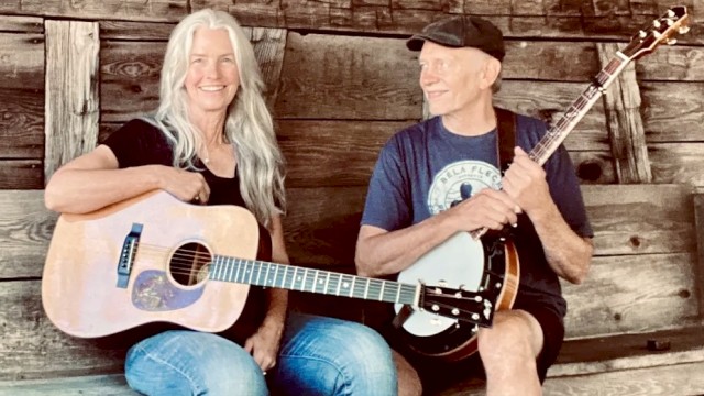 Female guitarist and male banjo player performing acoustic bluegrass music seated outdoors in rustic setting play Currents at Riverhouse on June 12