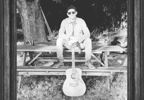 Male musician seated outdoors with acoustic guitar in black and white portrait style setting