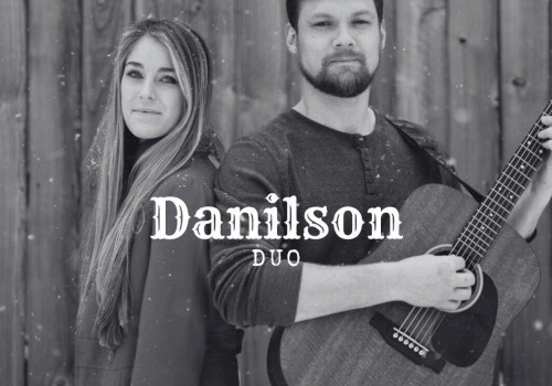 Male and female musicians standing back to back with acoustic guitar in front of wooden wall performing live music at Riverhouse Lodge in Bend Oregon