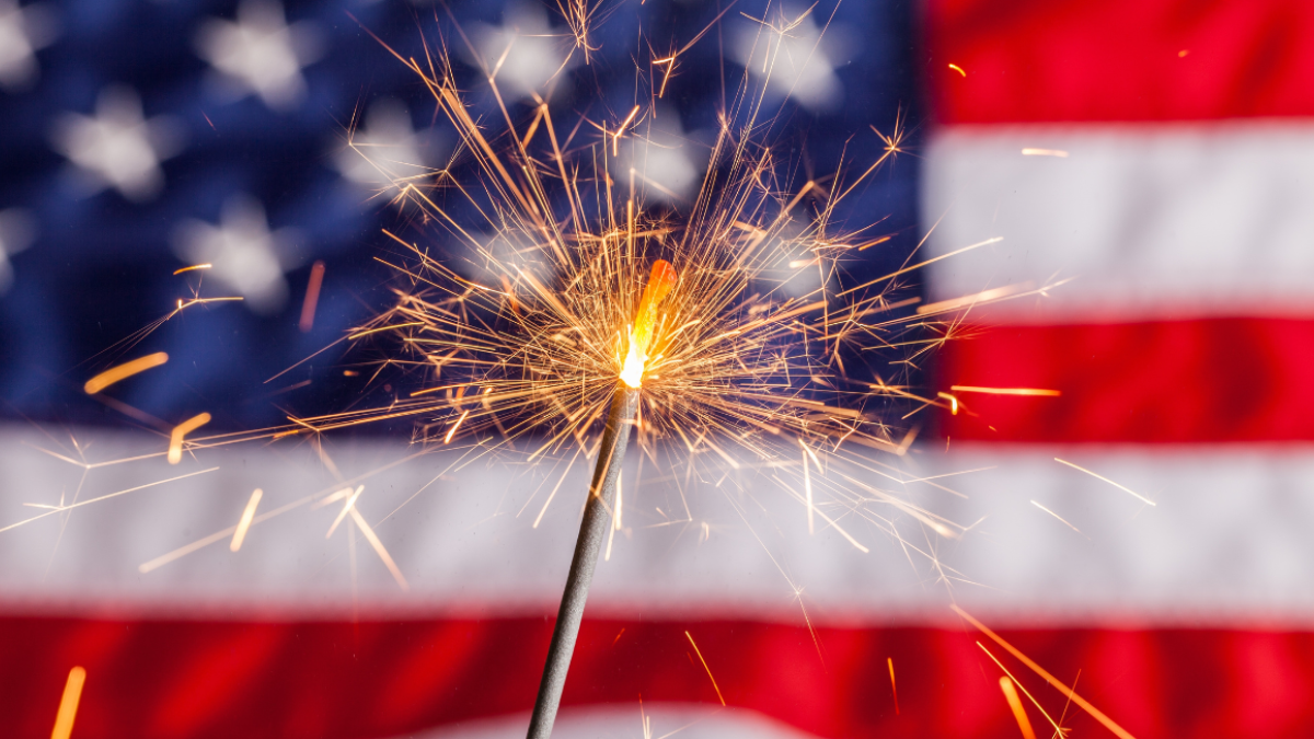 A sparkler burning in front of an American flag, celebrating independence or patriotic event. Spend Memorial Day at Riverhouse Lodge on the Deschutes river