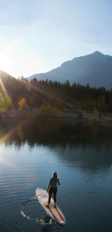 A person paddleboarding on a calm lake with mountains and the sunrise in the background.