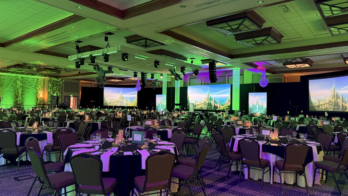 A large banquet hall decorated with multiple screens displaying a castle landscape, green and purple lighting, and round tables set for an event.