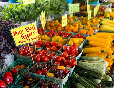 A market stand displays colorful fresh vegetables and a sign promoting mini bell peppers.