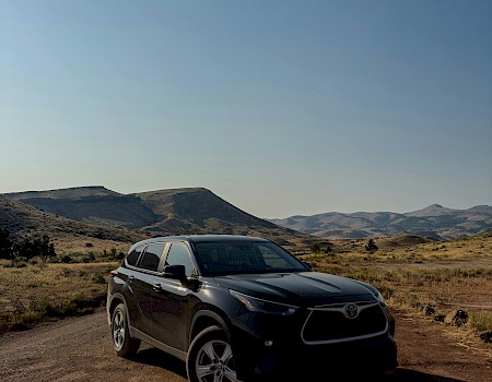 A black Toyota SUV parked on a dirt road in a mountainous, desert landscape with clear blue skies.