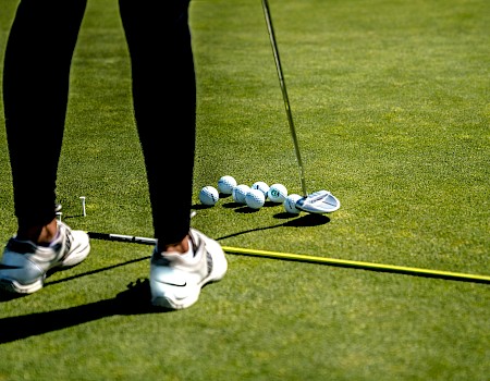 A golfer is preparing to hit the ball on a lush green golf course, surrounded by several golf balls, a club, and a measuring line.