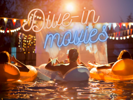 People are relaxing in floating tubes, watching a movie outdoors with colorful lights and a 
