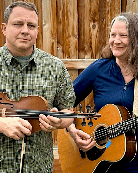 Two people, a man and a woman, are playing musical instruments outdoors in a backyard.