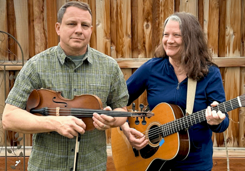 Two people, a man and a woman, are playing musical instruments outdoors in a backyard.