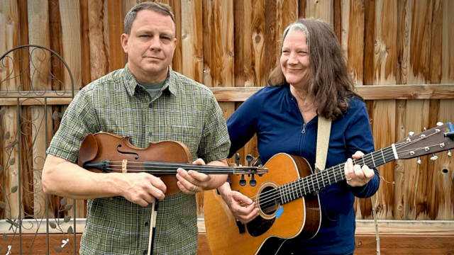 Two people, a man and a woman, are playing musical instruments outdoors in a backyard.