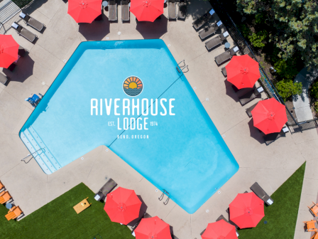 This is an aerial view of a swimming pool area with red umbrellas, lounge chairs, and lush greenery at the Riverhouse Lodge in Bend, Oregon.