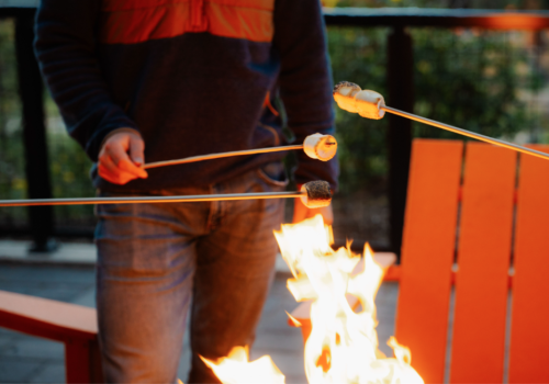 Guest roasting marshmallows over a fire pit at Riverhouse Lodge with signature orange chairs and Deschutes River views in the background during Stars & S’mores event.