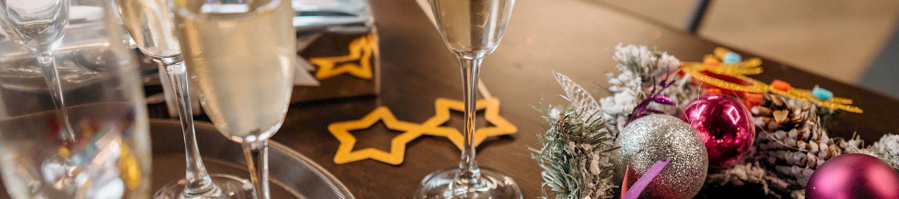 The image shows a table with several champagne glasses, some sparkling wine, and colorful Christmas ornaments and decorations.