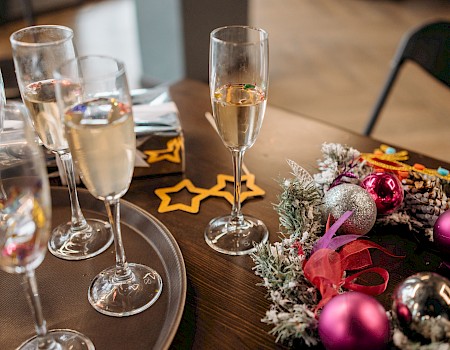 The image shows a table with several champagne glasses, some sparkling wine, and colorful Christmas ornaments and decorations.