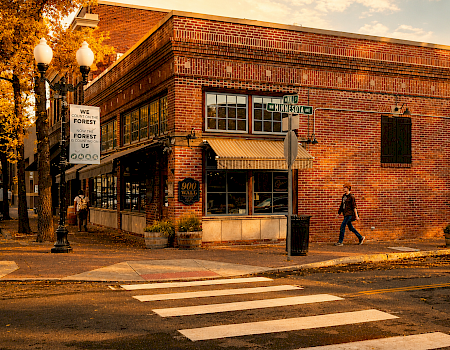 A person walks outside a brick building at the corner of NW Minnesota Ave and 900 Wall, with autumn trees and a sunset in the background.