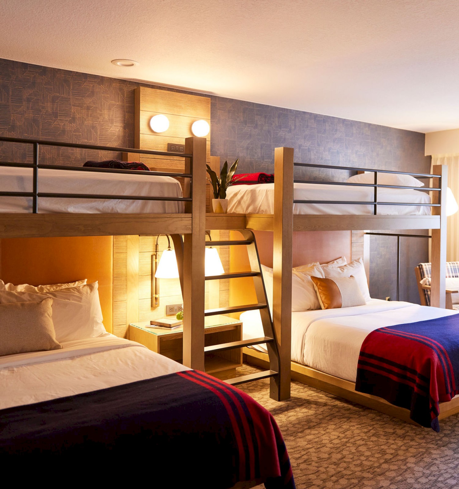 A hotel room with two beds, a bunk bed over the larger bed, a guitar, a chair, and a window with curtains.