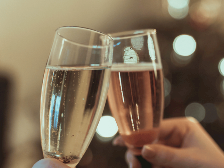 Two glasses of sparkling wine or champagne are being clinked together in a toast with blurred festive lights in the background.