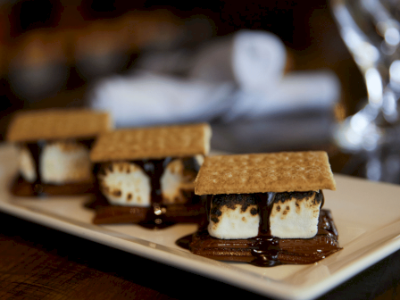 Three s'mores with graham crackers, toasted marshmallows, chocolate, topped with a cookie, on a white rectangular plate.