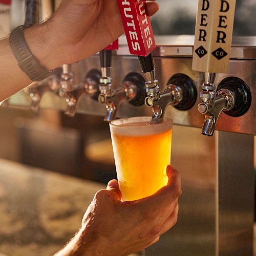 A hand is filling a glass with beer from a tap at a bar or brewery.