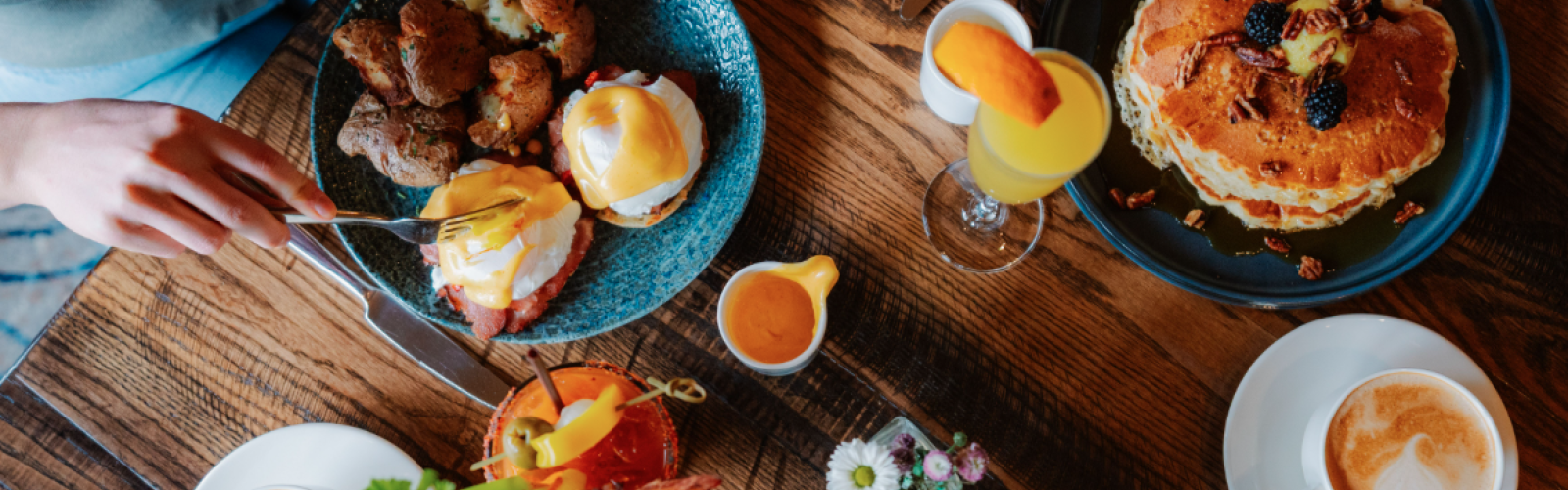 Overhead view of a hearty breakfast spread at Currents Restaurant & Lounge at Riverhouse Lodge in Bend, Oregon, featuring pancakes, eggs Benedict, coffee, and mimosas as part of the Bed & Breakfast hotel offer.