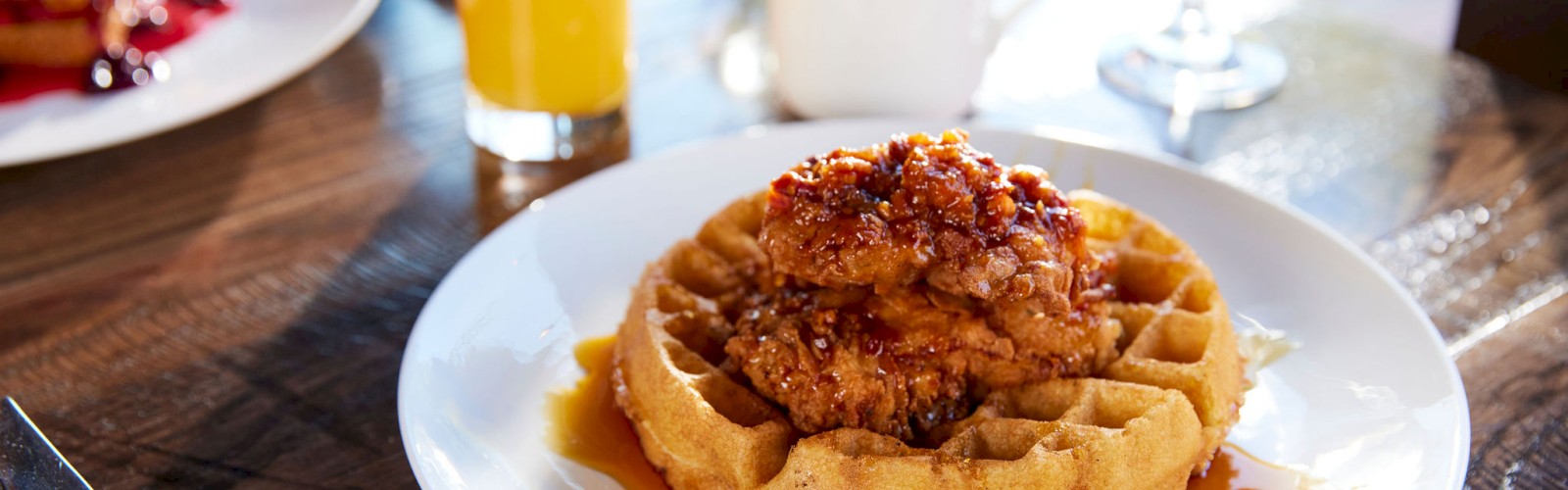 A plate of waffles topped with fried chicken and syrup, accompanied by a glass of orange juice, a coffee cup, and a water glass on a table.