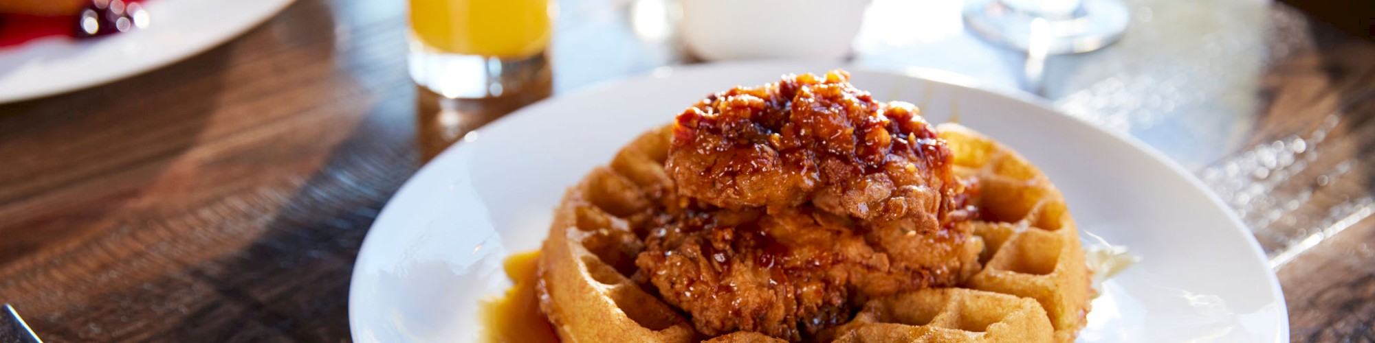 A plate of waffles topped with fried chicken and syrup, accompanied by a glass of orange juice, a coffee cup, and a water glass on a table.