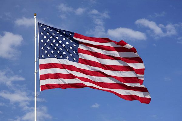 The image shows the United States flag waving in the wind against a blue sky with some clouds.