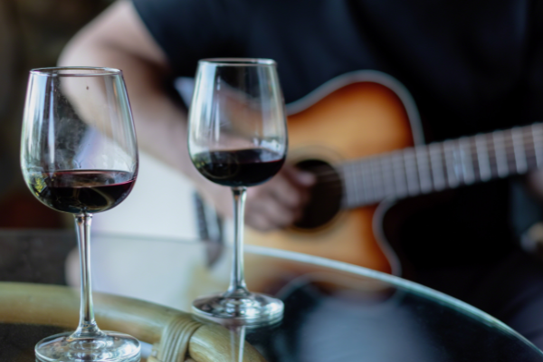 Two glasses of red wine on a table with a person playing a guitar in the background. Live music every Friday from 7-9 at Currents at Riverhouse Lodge in Bend Oregon