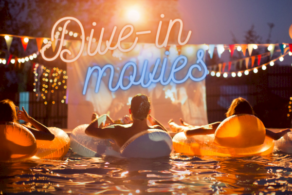 People in a pool watch a movie on a screen, with neon text saying 