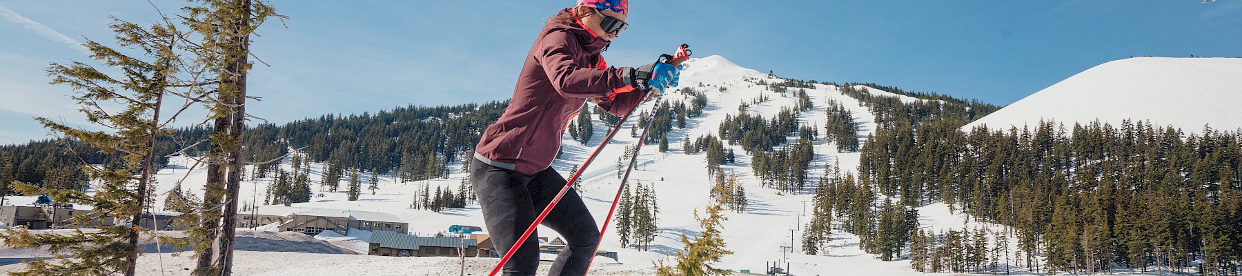 A person cross-country skiing in a snowy mountain landscape under a clear blue sky.