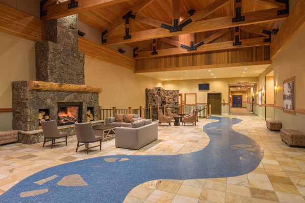 A cozy lobby with a stone fireplace, comfy seating, and a unique blue pathway in a wooden-beamed room, leading to a hallway and other rooms.